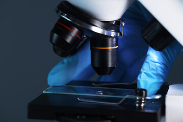 Scientist working with microscope on dark background, closeup