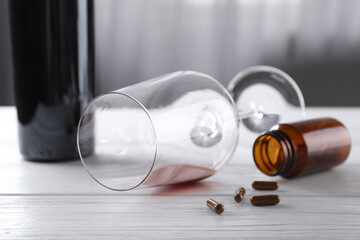 Alcohol and drug addiction. Overturned glass with red wine, bottle and pills on white wooden table,...