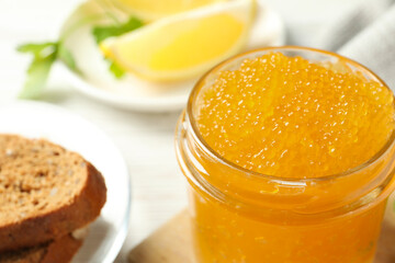 Fresh pike caviar in glass jar and bread on white wooden table, closeup