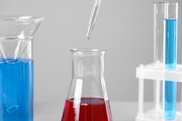 Dripping liquid from pipette into flask on grey background, closeup
