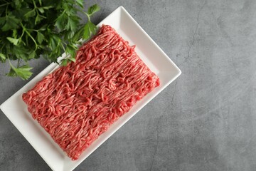 Raw ground meat and parsley on grey table, top view. Space for text
