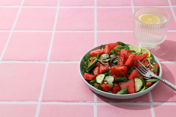 Watermelon salad in a bowl with a glass of lemonade on a pink background