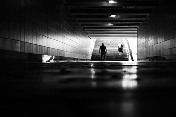 Back view of people in the city underpass. Exit from the subway. Street black and white photo. Typical urban scene. Abstract monochrome background. Light and shadow.