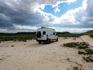 Solitary Camper Van Journey. A white Camper van parked on a sandy path near grassy hills under a cloudy sky. Parked in a desert.