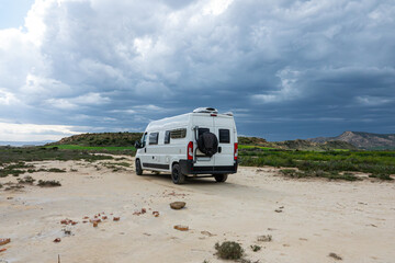 Solitary Camper Van Journey. A white Camper van parked on a sandy path near grassy hills under a cloudy sky. Parked in a desert.