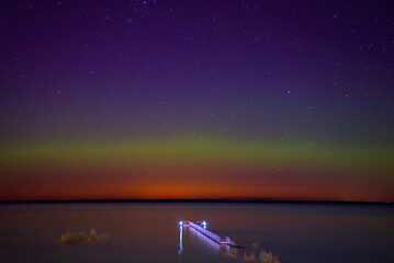 northern lights on a lake with a flooded boardwalk on a spring evening and an island of herbs