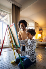 African american single mother with son drawing on board with chalks together. Family love concept.
