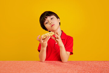 L:ittle Korean 7 years old boy, child in red polo shirt sitting at table, holding instant noodles...
