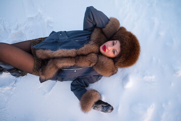 a beautiful girl in a fur jacket and hat walks and has fun in the winter forest.