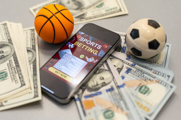 Smartphone with gambling mobile application and basketball ball with money close-up. Sport and betting concept