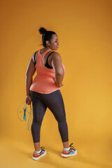 Jumping rope, standing. African American woman is in the studio against yellow background