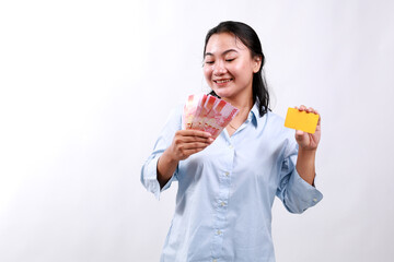 Happy asian woman holding credit card and Indonesian money rupiah, smiling, posing against white studio background