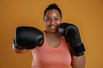 Boxer is ready to fight. African American woman is in the studio against yellow background