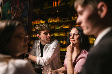 Positive young people enjoy communication and drinks in favourite pub. Young people locate near bar...