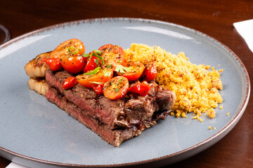 two pieces of sirloin steak cooked with fat, cherry tomato salad and farofa at a steakhouse dinner, close up