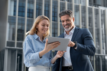 Mature 40s years old man, young adult woman employee discussing project on digital pc tablet...