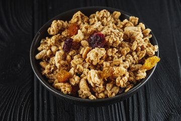 tasty crunchy granola with dried fruits on a black wooden rustic background