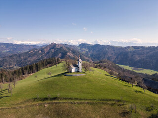 Stunning panoramic view of Julian Alps with iconic hilltop church of Saint Thomas in Slovenia, drone shot. Travel, nature, and landmarks concepts.