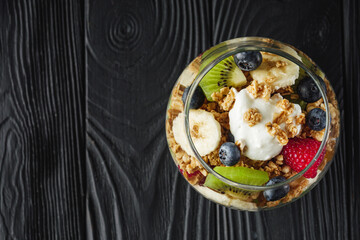 delicious crunchy granola dessert with berries and fruits on a black wooden rustic background