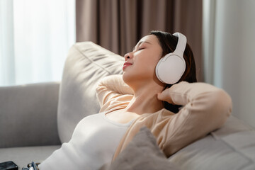 A woman is wearing headphones and laying on a couch