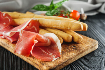 crispy grisini with prosciutto on a black wooden rustic background