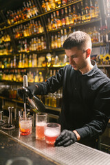 Concentrated bartender fills glasses with alcoholic beverages. Barman uses metal siphon standing...