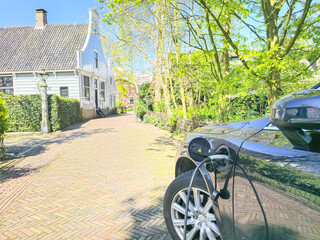 An electric EV car, shining under the sun, sits gracefully parked in front of a charming house in a...