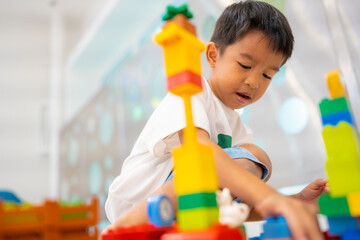 Adorable asian kindergarten boy enjoying play toy train block on white room
