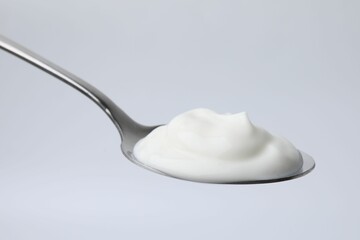Delicious natural yogurt in spoon on light background