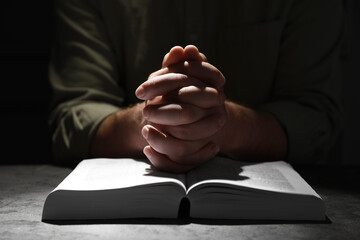 Religion. Christian man praying over Bible at table, closeup