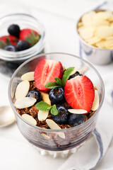 Tasty granola with berries, jam and almond flakes in glass on white table, closeup