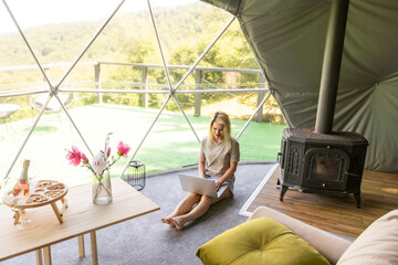 Transparent bubble tent at glamping, Lush forest around and interior. Woman with laptop