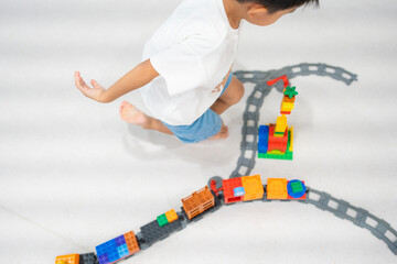 Adorable asian kindergarten boy enjoying play toy train block on white room