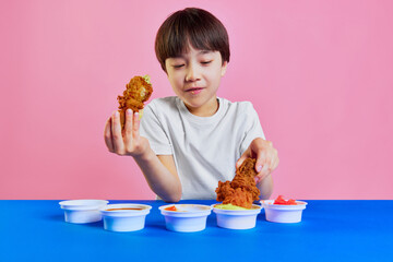 Little boy, Korean kid sitting at table and eating fried chicken, dipping in different sauces...