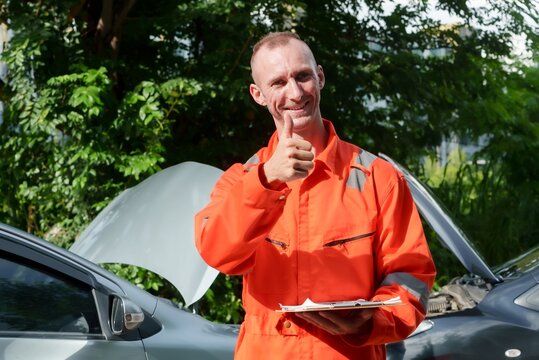 Man in high-visibility uniform gives a thumbs-up, holding a clipboard, car bonnet open behind, green foliage around. Smiling male in protective workwear approves with a thumb up, clipboard in hand