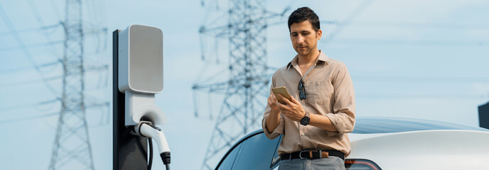 Man pay for electricity with smartphone while recharge EV car battery at charging station connected...