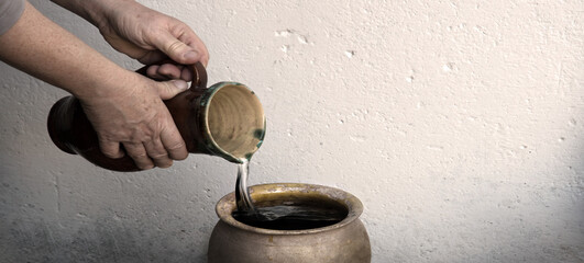 A hand holds a clay jar and pours water