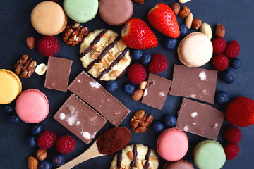 Macarons, chocolate, cookies, berries and various nuts on dark blue background. Top view.