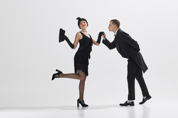 Man in classic black tuxedo and woman in flapper dress performing Charleston dance isolated against...