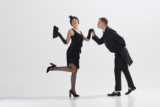 Man in classic black tuxedo and woman in flapper dress performing Charleston dance isolated against white studio background. Concept of art, retro and vintage, hobby, entertainment, 20s
