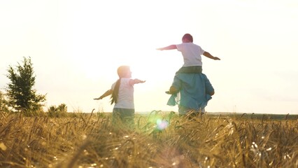 Happy family running at sunset dry wheat field with open hands flying imagination back view. Cheerful mother father and son fooling playing together flight fantasy imagine freedom happiness and unity