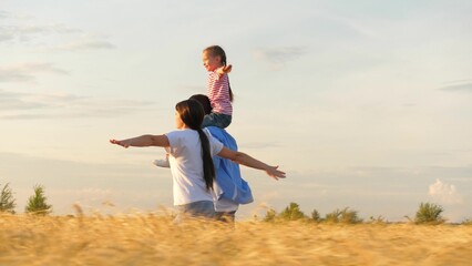 Family running flying plane imagination at sunset dry wheat field side view tracking shot. Happy mother father and daughter playing aeroplane with open hands relaxing together enjoy freedom