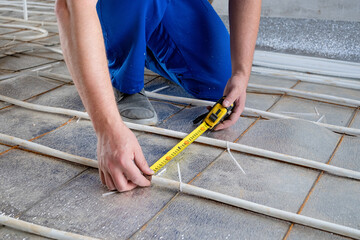 man worker takes measurements during the installation of a warm floor