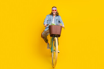 Full size photo of cool young man enjoy ride bicycle wear denim shirt isolated on yellow color background