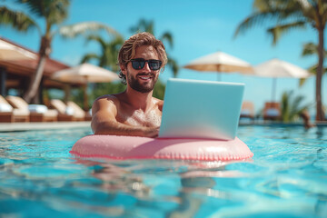 happy male freelancer in sunglasses working on laptop swimming in pool on a pink swimming circle
