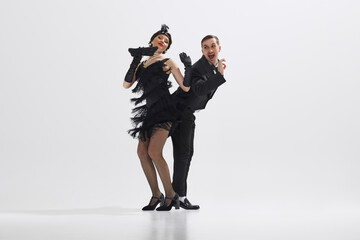 Young stylish man and woman dressed in 1920s attire perform lively Charleston dance isolated over...