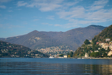 Mesmerizing view of the lake of Como over Alpine mountains background. Clear water of the lake reflecting floating boats and houses on the waterfront. Italy. Nature background, Tourism and travel.