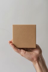 Hand holding a square brown paper box in front of beige background