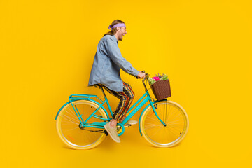 Full size profile photo of cool young man ride bicycle wear denim shirt isolated on yellow color background