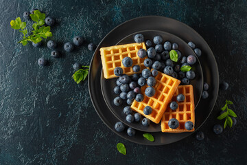 Belgian waffles with blueberries on a black plate.